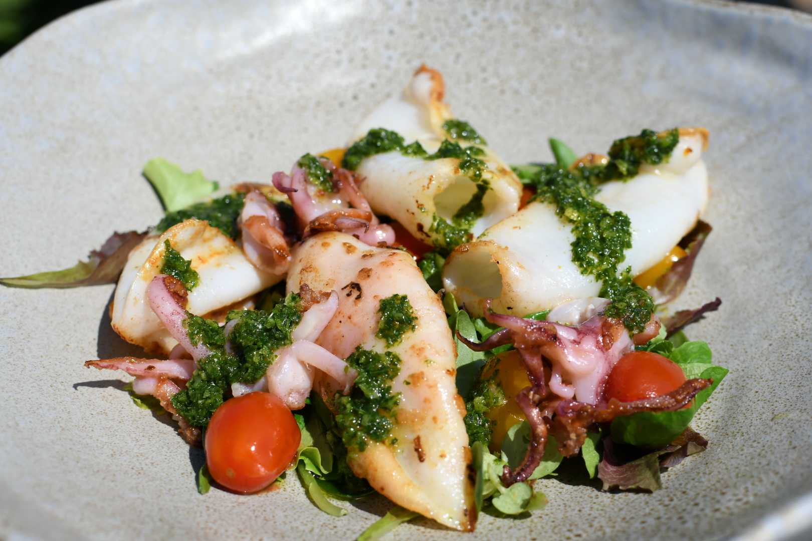 Calamaro alla griglia servito su insalatina con datterini confit e dressing al limone conservato.