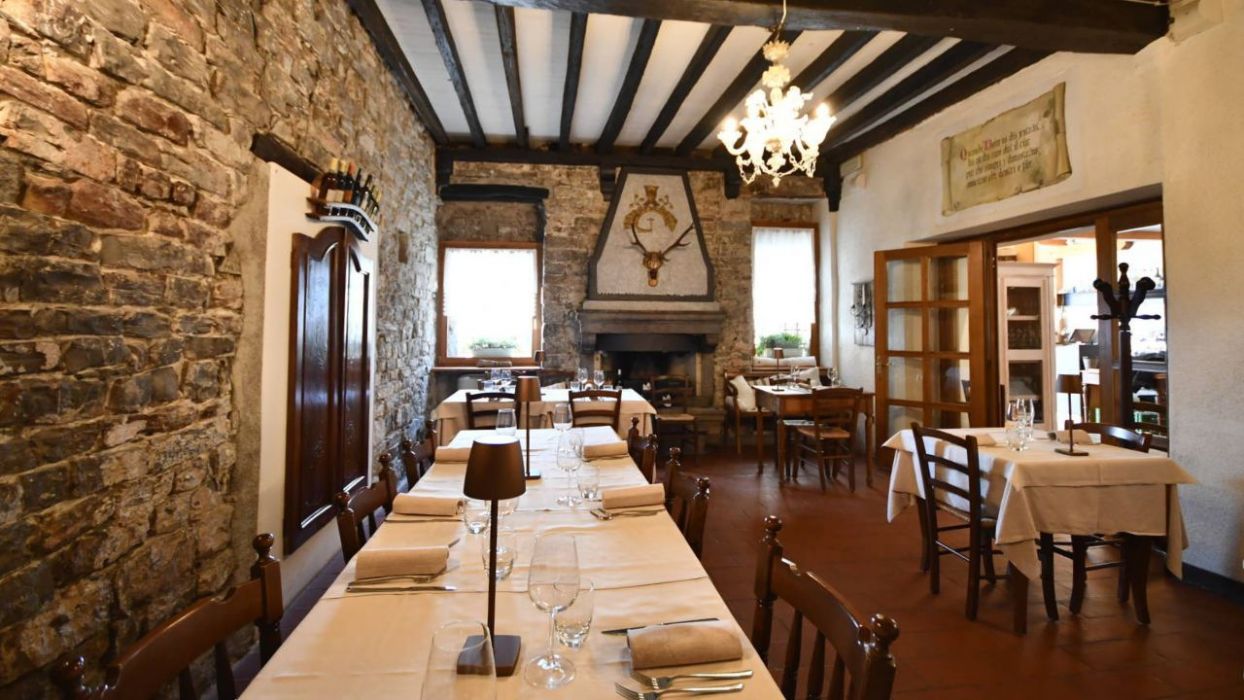 La sala interna dell’Osteria Solder accoglie con calore e tradizione: muri in pietra, travi a vista, camino e arredi in legno creano un’atmosfera intima e autentica, perfetta per vivere la convivialità friulana in un ambiente elegante e familiare.