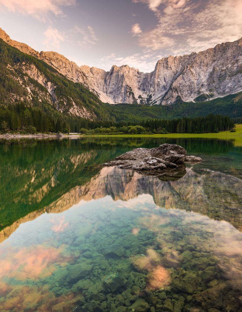 Il Lago di Fusine riflette come uno specchio le vette maestose delle Alpi Giulie, tra boschi verdi e cieli dorati dal tramonto. Un luogo incantato del Friuli Venezia Giulia, dove natura incontaminata e silenzio regalano pura meraviglia.